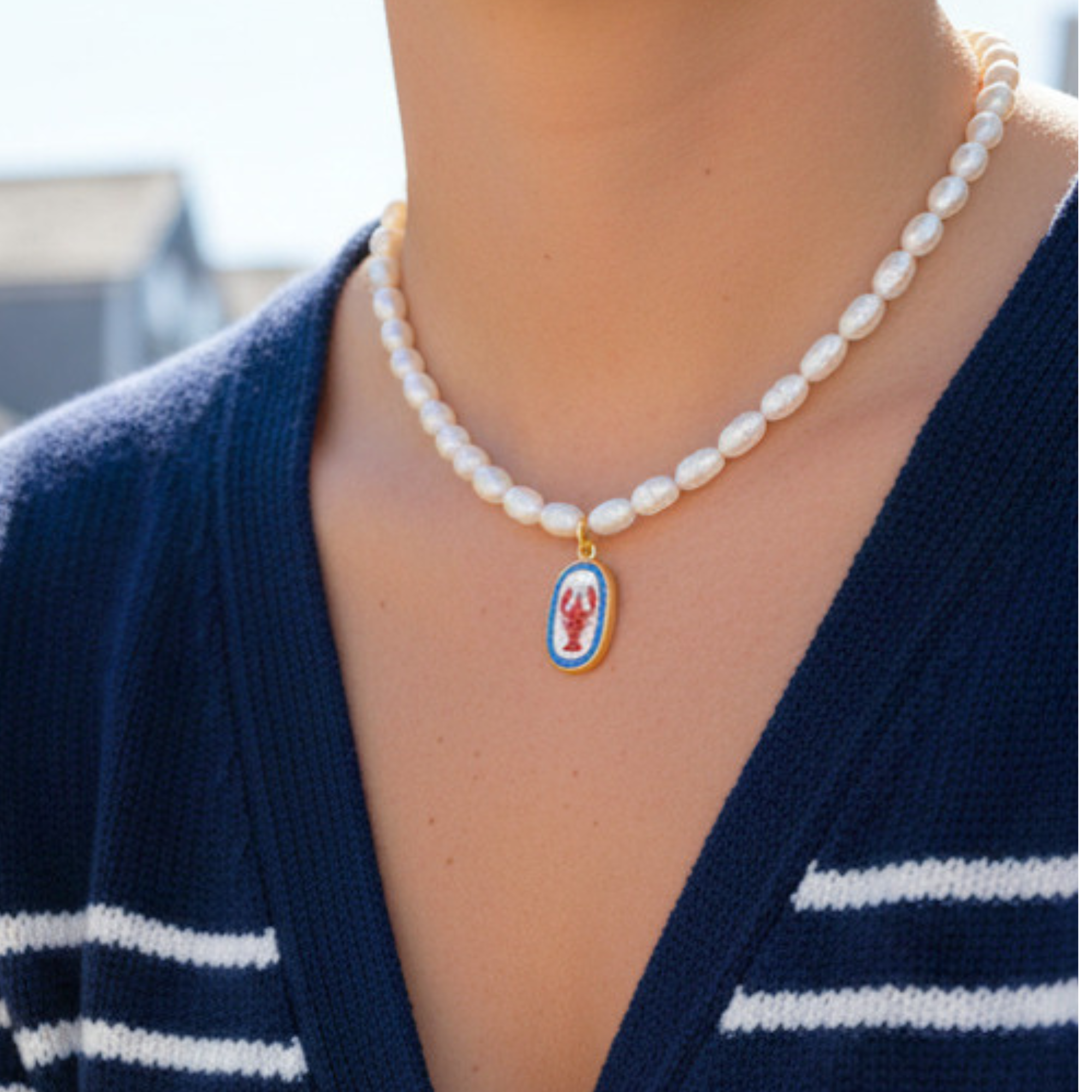 Pearl necklace with a lobster pendant worn by a person in a blue cardigan.