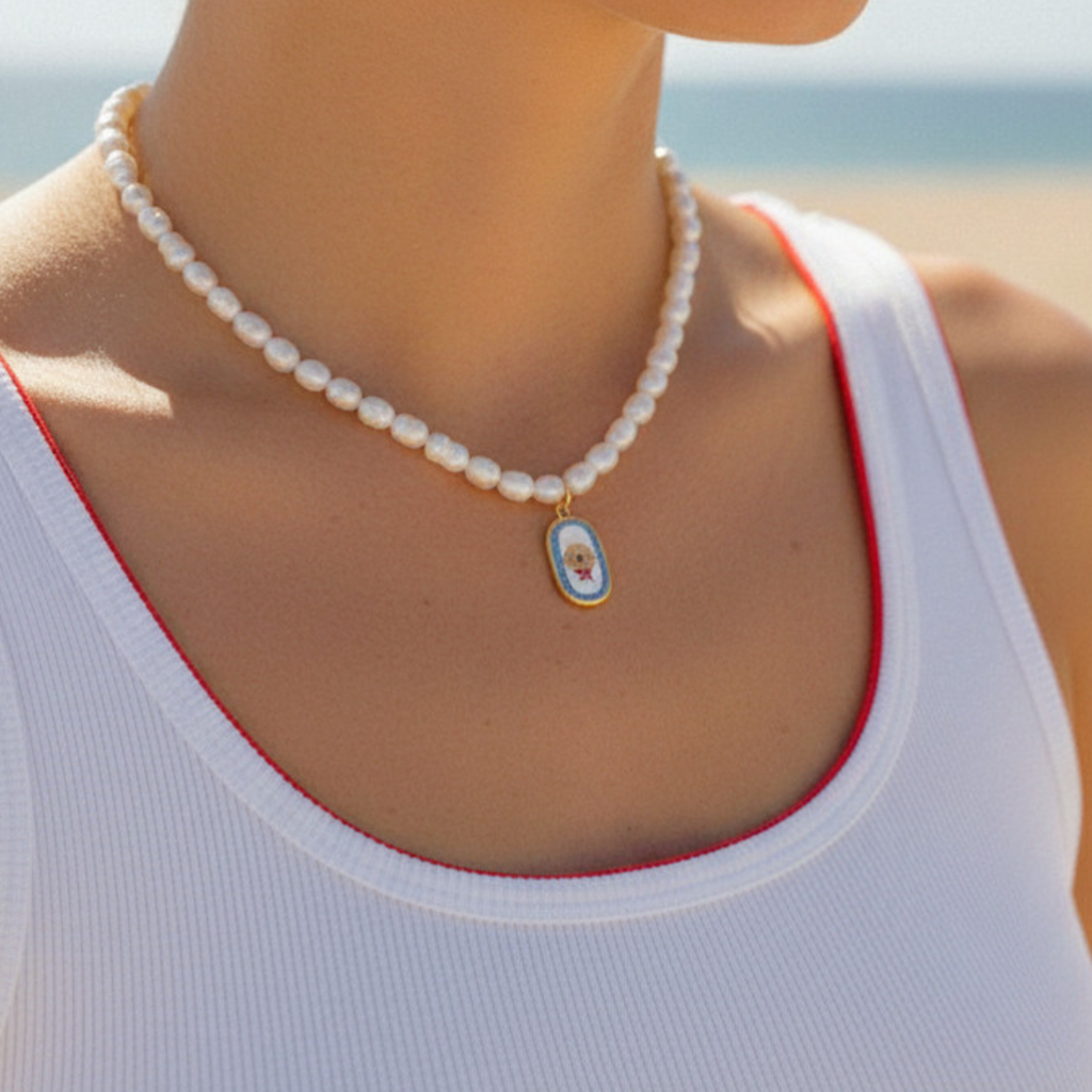 Pearl necklace with a golden retriever dog pendant charm worn by a person on a beach.