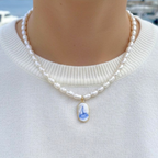 Pearl necklace with a sailboat pendant charm on a white sweater